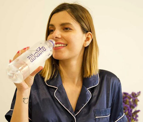 woman drinking a 600ml bottle of alkaline water at home